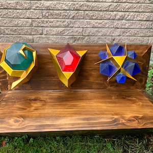 May include: Wooden bench with three geometric shapes. The shapes are a green gem, a red gem, and a blue starburst, each with gold accents. The bench is stained a dark brown color.