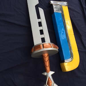 May include: A silver sword with a copper-colored handle and a blue and yellow scabbard. The sword has a decorative design on the blade and a pointed tip.