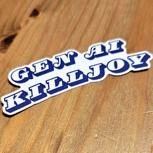 Könnte beinhalten: Ein weißer Aufkleber mit blauer Schrift, der "GEN AI KILLJOY" in einer stilisierten Schriftart zeigt. Der Aufkleber befindet sich auf einer Holzoberfläche mit sichtbarer Holzmaserung.