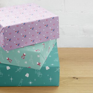 Peut inclure: Trois boîtes cadeaux enveloppées de papier à motifs. La boîte supérieure est lavande avec un motif répété de fées des dents, de dents et de rubans roses. La boîte du milieu est turquoise avec des dents, des rubans et le texte "Tooth Fairy Gifts". La boîte du bas est turquoise avec des dents et des étoiles.