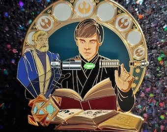Può includere: Uno spillo in smalto dorato con il ritratto di un giovane cavaliere Jedi che tiene una spada laser e un libro. Lo spillo è su uno sfondo blu con accenti dorati e un bordo decorativo.
