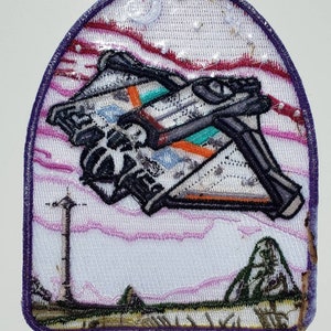 May include: Embroidered patch featuring a white spaceship with orange and teal accents flying over a pink and purple landscape. The patch has a purple border and is sewn onto a white background.