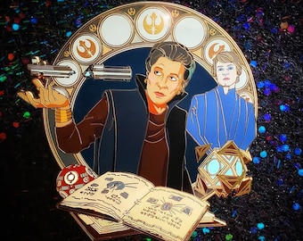 Può includere: Spilla smaltata con la Principessa Leia e Anakin Skywalker di Star Wars. La spilla ha un bordo dorato con sfondo blu e bianco. Leia tiene una spada laser. Altri elementi includono un droide, un libro e un oggetto geometrico.