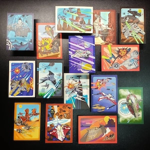 Puede incluir: Un conjunto de 14 cartas coleccionables que presentan varias naves espaciales de Star Wars, incluyendo X-wings, cazas TIE y el Halcón Milenario. Las cartas son coloridas y presentan ilustraciones detalladas de las naves espaciales.