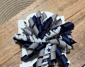 May include: A white, gray, and navy blue hair bow with a Dallas Cowboys logo and the word "Boys" printed on it.