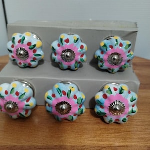 May include: Six ceramic drawer knobs with a floral design. The knobs are painted in shades of blue, pink, yellow, and green. Each knob has a silver metal base.