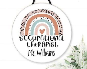 May include: A white round sign with a rainbow design and leopard print accents. The sign reads "Occupational Therapist Ms. Williams".