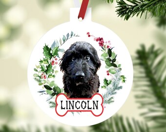 May include: White round Christmas ornament featuring a black dog with a floral wreath and the name "LINCOLN" in a bone-shaped design. The ornament hangs from a red and white ribbon, perfect for pet lovers.