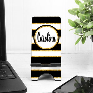 May include: Black and white striped phone stand with gold glitter accents. The stand has a circle with the name "Carolina" in a gold glitter circle.