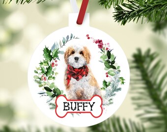 May include: White round Christmas ornament featuring a watercolor illustration of a dog wearing a red plaid scarf, surrounded by a wreath of holly and berries. The dog's name, "BUFFY," is displayed on a bone-shaped tag.