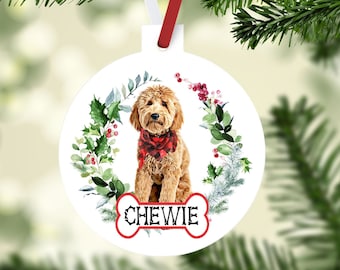 May include: White round Christmas ornament featuring a golden doodle dog wearing a red and black plaid scarf. The dog's name, "Chewie," is displayed on a bone-shaped tag. The ornament is decorated with a green and red floral wreath and a red ribbon.