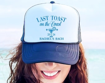 May include: A white and navy blue trucker hat featuring the text "LAST TOAST on the Coast" in light blue, a cocktail graphic, and the year 2024. The hat also includes the text "RACHEL'S BACH".