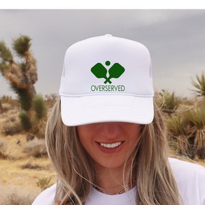 May include: White trucker hat with a green logo of two pickleball paddles and the text "OVERSERVED".