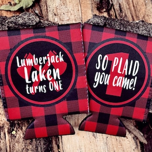 May include: Two red and black plaid beverage insulators with a white circle on each. The left insulator says "Lumberjack Laken turns one". The right insulator says "So plaid you came!"