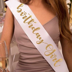May include: White satin sash with gold lettering that reads "Birthday Girl".
