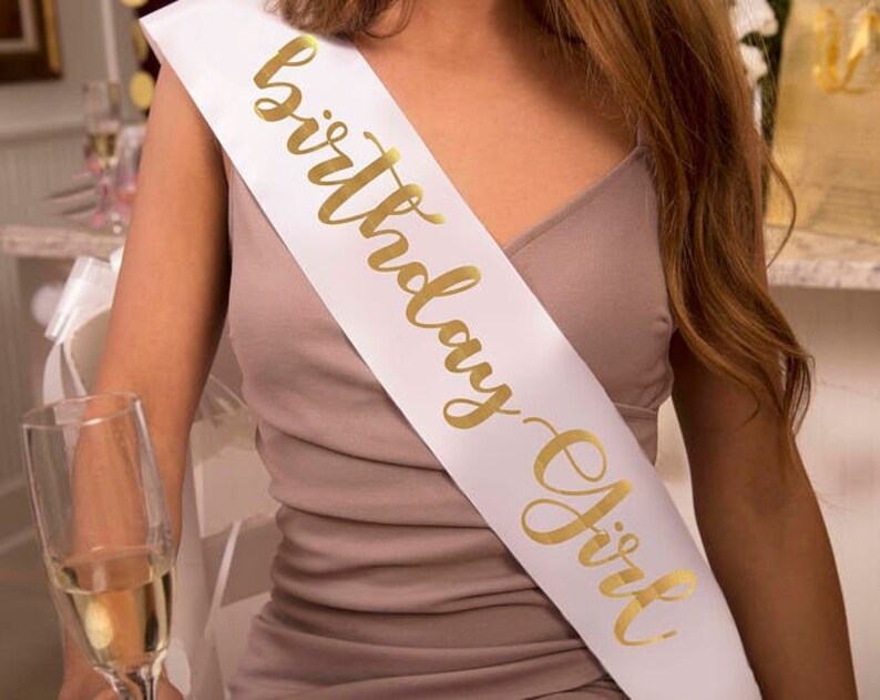 May include: White satin sash with gold lettering that reads "Birthday Girl".