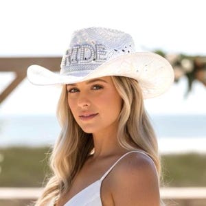 K&ouml;nnte beinhalten: Wei&szlig;er Cowboyhut mit dem Wort "RIDE" in silbernen Buchstaben geschrieben. Der Hut hat ein perforiertes Design und eine breite Krempe. Der Hut ist ein Hochzeitsaccessoire.