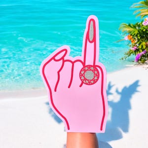 May include: Pink foam hand with a red outline and a large silver glitter ring on the middle finger. The ring has a red center.