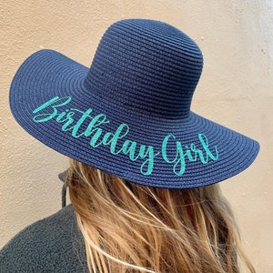 May include: A navy blue sun hat with a wide brim and a turquoise inscription that reads "Birthday Girl".
