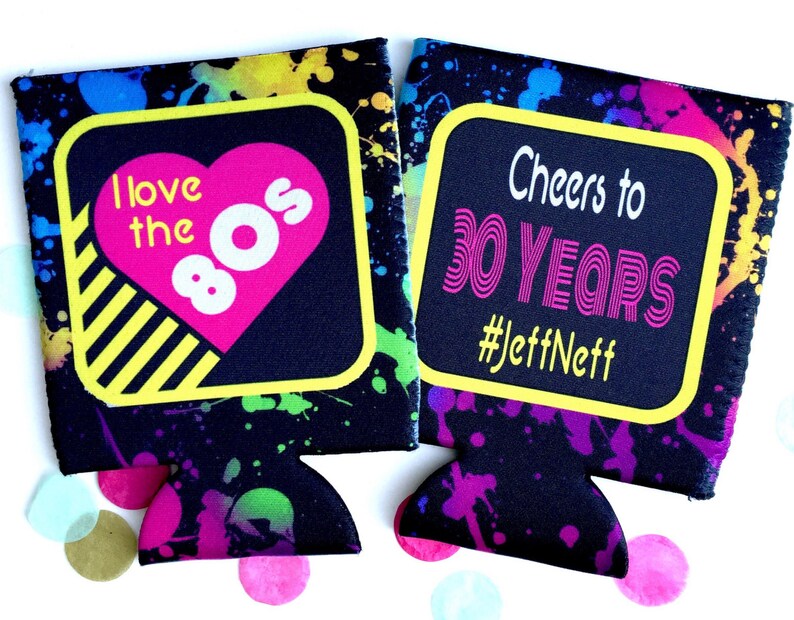 May include: Two black neoprene can coolers with a colorful paint splatter design. One cooler says "I love the 80s" with a pink heart and the other says "Cheers to 30 Years #JeffNeff".