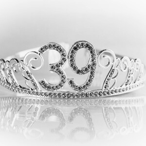 May include: A silver tiara with the number "39" prominently displayed in the center. The tiara is adorned with sparkling rhinestones and has a reflective surface below.