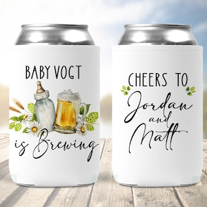 Puede incluir: Dos enfriadores de latas blancos con tem&aacute;tica de baby shower. Un enfriador dice "Baby Vogt is Brewing" con una ilustraci&oacute;n de biber&oacute;n y jarra de cerveza. El otro enfriador dice "Cheers to Jordan and Matt".
