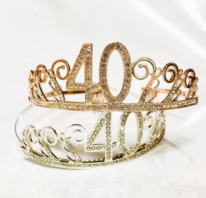 May include: Two decorative tiaras, one gold and one silver, each featuring the number "40" encrusted with rhinestones. The gold tiara is on top, with a delicate, scrolled design. The silver tiara is below, with a similar design.