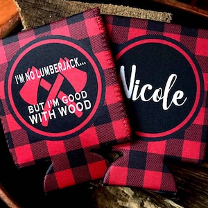 May include: Two red and black buffalo plaid can coolers. One cooler has the text "I'm no lumberjack... But I'm good with wood" with two crossed axes. The other cooler has the name "Nicole" in white cursive.