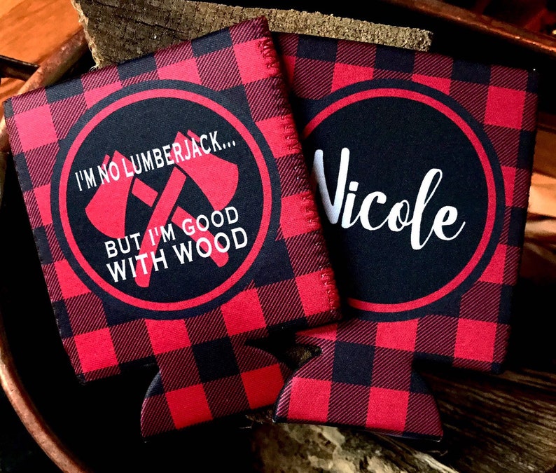 May include: Two red and black buffalo plaid can coolers. One cooler has the text "I'm no lumberjack... But I'm good with wood" with two crossed axes. The other cooler has the name "Nicole" in white cursive.