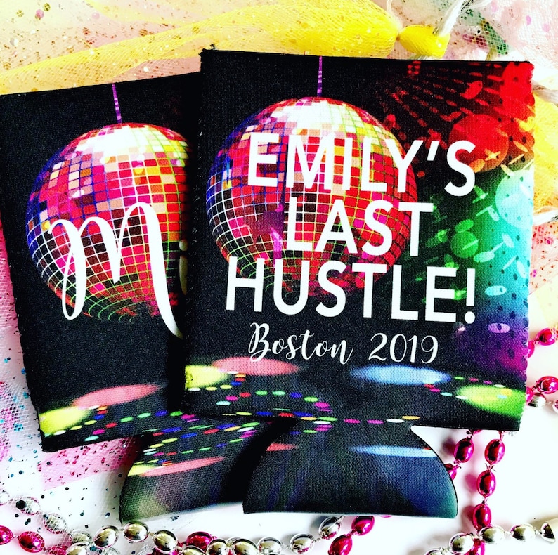 May include: Two black can coolers with a disco ball design. One cooler features a large white "M", the other reads "EMILY'S LAST HUSTLE! Boston 2019" in white. The disco balls are multi-colored, with red, yellow, and blue hues.