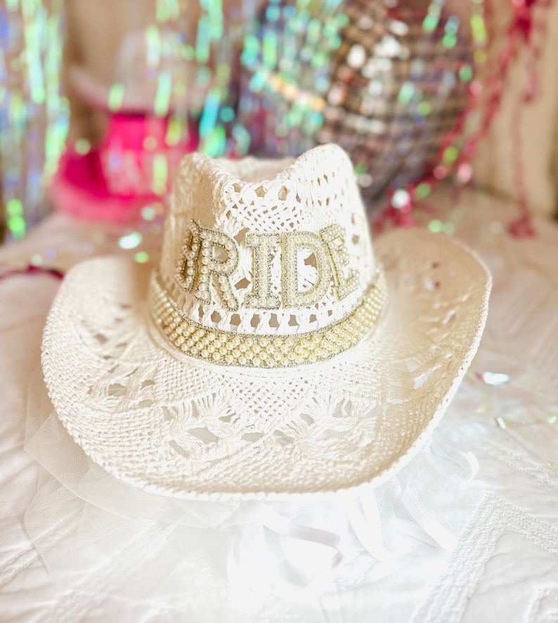 May include: White crochet cowboy hat with a pearl trim and the word "BRIDE" in rhinestones.