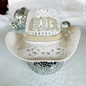 May include: White crochet cowboy hat with a pearl trim and the word "BRIDE" spelled out in rhinestones.