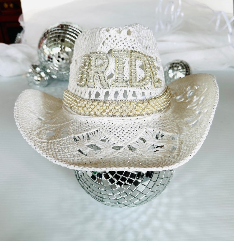 May include: White crochet cowboy hat with a pearl trim and the word "BRIDE" spelled out in rhinestones.