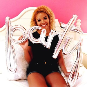 May include: A person holding silver foil balloons that spell out "party" in front of a pink wall.