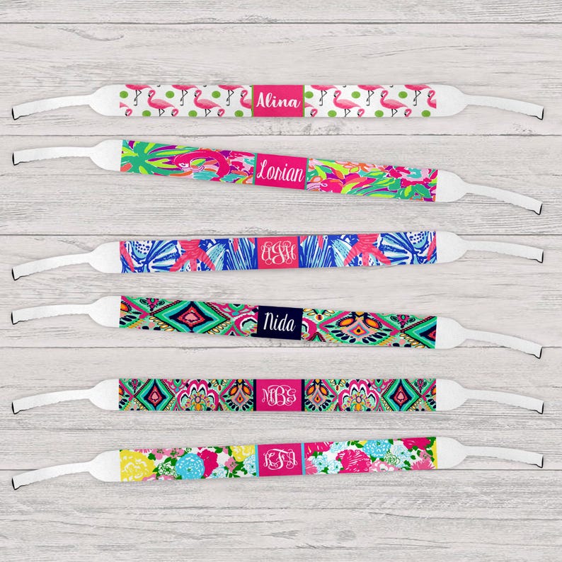 May include: A collection of colorful eyeglass straps with various patterns, including flamingos, floral designs, and geometric shapes. Each strap features a personalized name or initials on a rectangular label. The straps have white adjustable ends.
