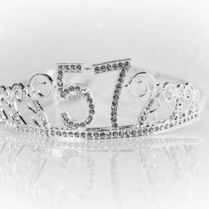 May include: A silver tiara with rhinestones, featuring the numbers 57. The tiara is on a white background.