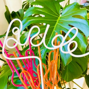 May include: White neon sign that says "relax" with pink and orange drinking straws in the background.