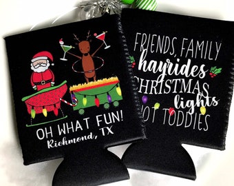 May include: Black and white Christmas-themed can cooler with a Santa Claus, reindeer, and a wagon with lights. The text reads "FRIENDS, FAMILY hayrides CHRISTMAS lights HOT TODDIES" and "OH WHAT FUN! Richmond, TX".