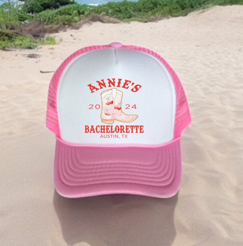 May include: Pink trucker hat with a white front panel featuring the text "Annie's 20 24 Bachelorette Austin, TX" and a pair of pink cowboy boots with red accents.
