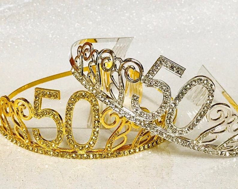 May include: Two gold and silver tiaras with rhinestones and the number 50 on them. The tiaras are decorated with swirls and are perfect for a 50th birthday party.