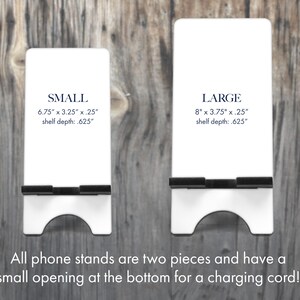 Puede incluir: Dos soportes blancos para tel&eacute;fono, etiquetados como "SMALL" y "LARGE", con bordes de soporte negros. El soporte "SMALL" mide 17.1 cm x 8.3 cm x 0.6 cm, y el soporte "LARGE" mide 20.3 cm x 9.5 cm x 0.6 cm. Ambos tienen una abertura inferior para un cable de carga.