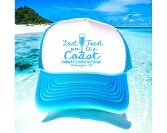 May include: A white and blue trucker hat with the text "Last Toast on the Coast" and "Carmen's Bach Weekend Wilmington, NC". The hat has a blue mesh back and a white front.
