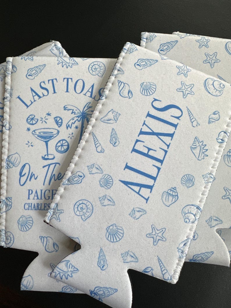 May include: White foam can coolers featuring a blue seashell and starfish pattern. One cooler displays the text LAST TOAST, a cocktail glass, a palm tree, and the names PAIGE and CHARLES. Another cooler features the name ALEXIS in blue text.