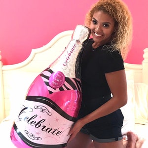 May include: A pink and black foil balloon shaped like a champagne bottle with the words "Celebrate" and "The Very Best" printed on it.
