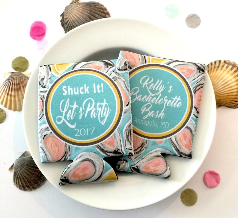 May include: Two blue and white can coolers with oyster shell designs and the text "Shuck It! Let's Party 2017" and "Kelly's Bachelorette Bash Annapolis, MD". The coolers are on a white plate with seashells and confetti.
