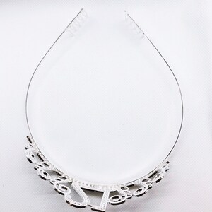 May include: A silver tiara with a decorative design at the base. The tiara has a clear plastic band for securing it to the head. The design includes the letters "J" and "S".