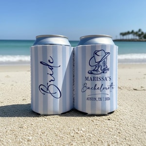 May include: Two blue and white striped can coolers on a sandy beach. One cooler says "Bride" in cursive, the other says "Marissa's Bachelorette" with a cowboy boot and hat graphic, and "Austin, TX | 2026".