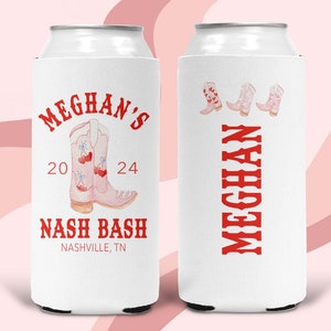 May include: White can cooler with a red and pink design. It features the text "Meghan's 20 24 Nash Bash Nashville, TN" and a pair of pink cowboy boots with cherries. The other side of the cooler has the text "Meghan" in red.