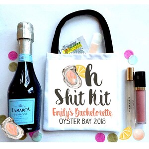 May include: A white tote bag with a black handle, featuring the text "Oh Shit Kit" and "Emily's Bachelorette Oyster Bay 2018". The image includes a bottle of Prosecco, confetti, and beauty products.