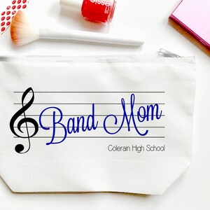 May include: White canvas cosmetic bag with a zipper closure. The bag features a musical staff with a treble clef and the words "Band Mom" in blue script. Below the text is "Colerain High School".